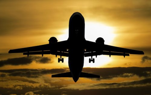 Silhouette of a large airplane flying against a dramatic sunset sky near Washington D.C., with the sun creating a bright halo effect behind the aircraft.
