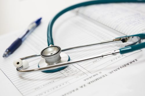 A stethoscope rests on an open medical document with a pen nearby, highlighting the tools used by professionals in the field. The image subtly underscores themes of healthcare and medical practices, where understanding the difference between malpractice and negligence is crucial.