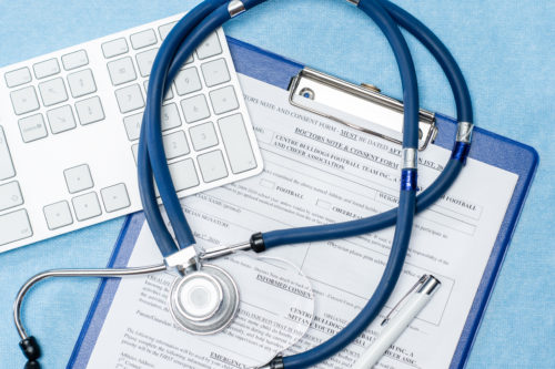 A stethoscope rests on a medical consent form attached to a blue clipboard, hinting at discussions about potential medical factors or causes of birth injuries. Nearby, a computer keyboard and pen lie on the light blue surface, ready for use.