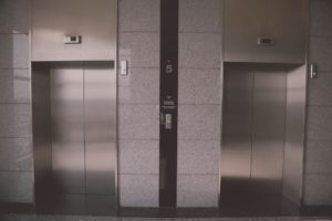 A pair of closed elevator doors on a gray tiled wall in Washington D.C. The number 5 is displayed between the doors, indicating the floor level. The panel shows up and down arrows for direction selection, reminding you that when it comes to elevator safety, knowing what you need to know is essential.