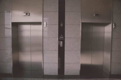 In a modern building in Washington D.C., two closed elevator doors stand surrounded by sleek gray stone tiles. A prominent sign marks the fifth floor, providing passengers with a sense of direction and what to do next.