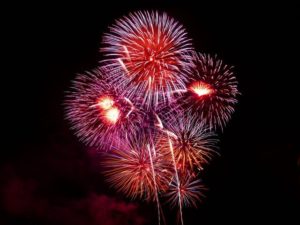 Colorful fireworks explode against a dark night sky, displaying vibrant hues of red, purple, and bright white. The dazzling show evokes the festive atmosphere of the 4th of July celebrations while highlighting the importance of firework safety amid the spectacle.