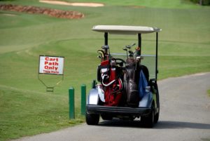 A golf cart filled with bags is parked on a path at a golf course, highlighting the need for golf safety. A sign reads, "Cart Path Only This Hole," warning of potential golf cart accidents. Lush greens and sand bunkers stretch into the distance.