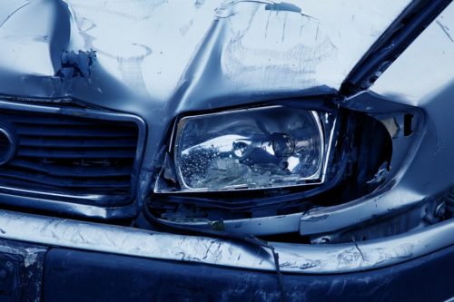 Close-up of a damaged car from a recent car accident, with a dented front and broken headlight. The metal is crumpled around the light, and there are visible scratches and marks on the bumper, highlighting potential grounds to seek legal action. The image shows signs of collision.