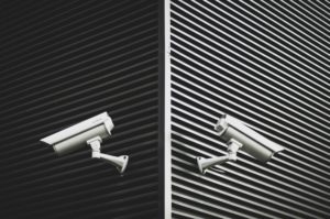 Two security cameras are mounted on the corner of a building in Washington D.C. The wall features a pattern of horizontal metal slats, creating a modern and industrial appearance. Positioned to monitor in opposite directions, they help prevent inadequate security incidents.