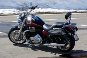 A black and red motorcycle with chrome details is parked on a paved road in Washington D.C. It features a leather saddlebag and backrest, perfectly framed against a backdrop of snow-covered ground.