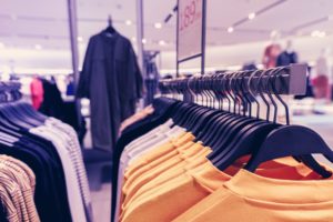 A clothing store rack showcases a variety of shirts in vibrant colors like yellow and white, set against blurred images of more hanging garments. The well-lit, inviting atmosphere emphasizes department store safety, ensuring a pleasant and secure shopping experience.