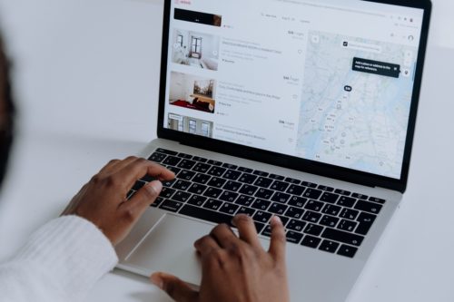 A person using a laptop browses a booking website, checking accommodations in Washington D.C., with prices and a map on the screen. The laptop keyboard is visible as they type, exploring what you should know about potential Airbnb accidents and safety measures.