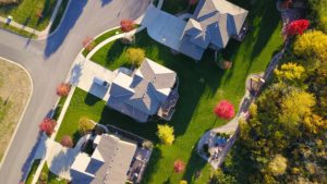 Aerial view of a suburban residential area near Washington D.C., featuring five houses with gray rooftops, neatly manicured green lawns, and colorful autumn trees. Curved streets and driveways create a winding pattern through the neighborhood, offering residents scenic views while protecting their legal rights.