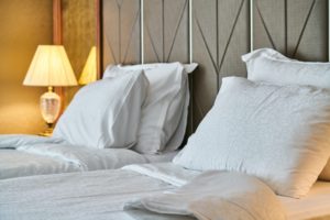 A cozy hotel room in Washington D.C. features two neatly made beds with white linens and pillows. A warm light from a decorative lamp on a bedside table illuminates the room, while the upholstered headboard adds a touch of elegance.