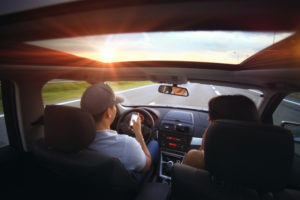 View from the backseat of a car, possibly an Uber, with a man driving and a woman in the passenger seat. The road ahead winds through Washington D.C., visible through the windshield as the sun sets, casting a warm glow on this tranquil scene.