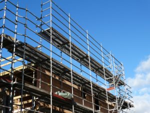 A construction site in Washington D.C. features metal scaffolding surrounding a building under clear blue skies. The structure is partially built with exposed bricks and wooden beams, serving as a reminder of the importance of safety measures to prevent scaffolding accidents.