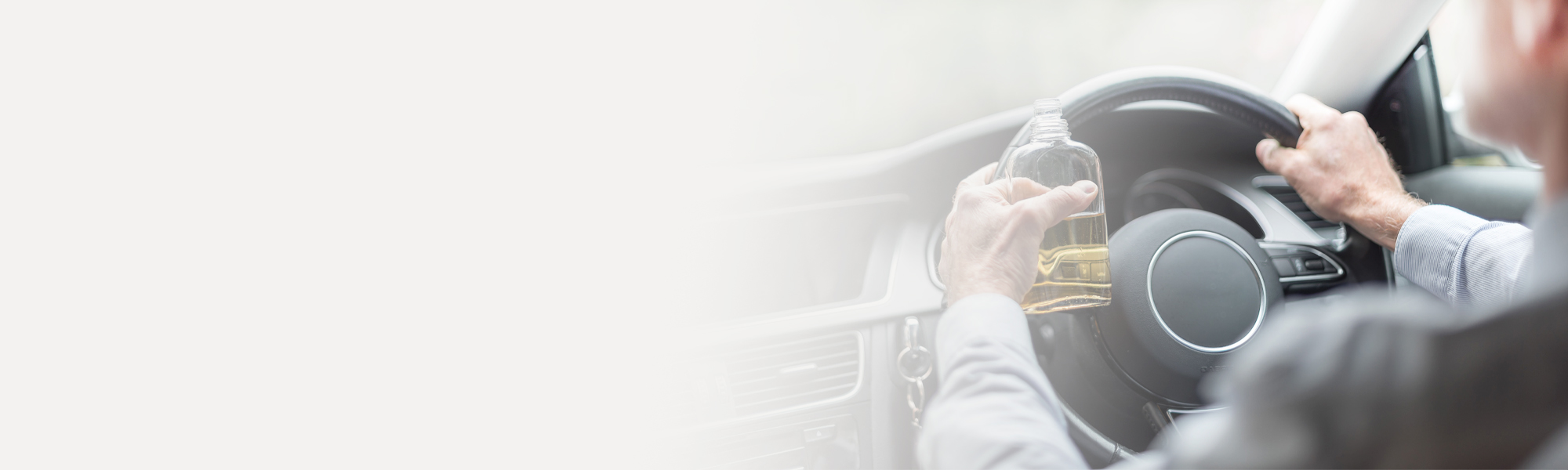 Person driving a car while holding a bottle with a light-colored drink, potentially indicating a dangerous situation. The background is blurred, emphasizing focus on the driver and steering wheel. Washington, D.C. Drunk Driving Accident Lawyer concept image