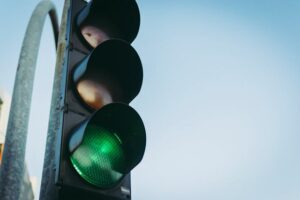Close-up of a traffic light with the green light illuminated, signaling "go," against a clear blue sky. Perched on a curved pole, it's a reassuring sight in contrast to stories of faulty traffic signals elsewhere.