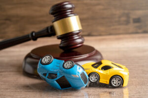 A judge's gavel rests behind two toy cars, one blue car flipped upside down and one yellow car upright, symbolizing a duty of care car accident and ensuing legal proceedings.